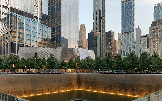 9/11 Memorial reflecting pool with museum entrance and skyscrapers in New York City.