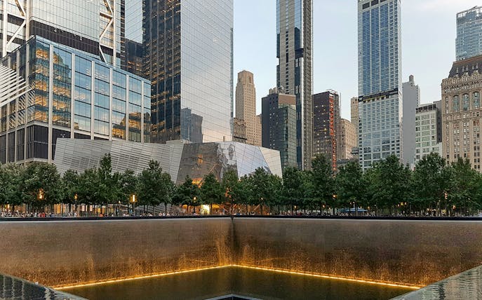 9/11 Memorial reflecting pool with museum entrance and skyscrapers in New York City.