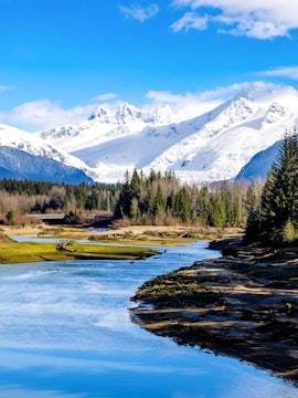 Mendenhall River flowing with snow-capped Mendenhall Glacier in Juneau, Alaska.