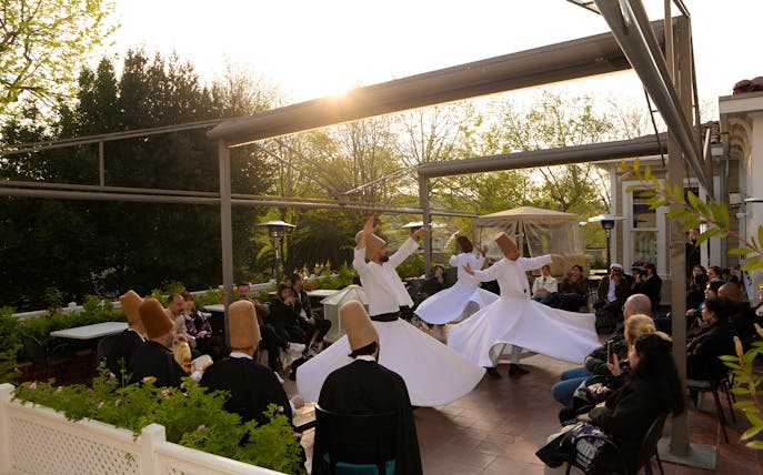 Whirling dervishes performing on a terrace with an audience, Hagia Sophia in the background.