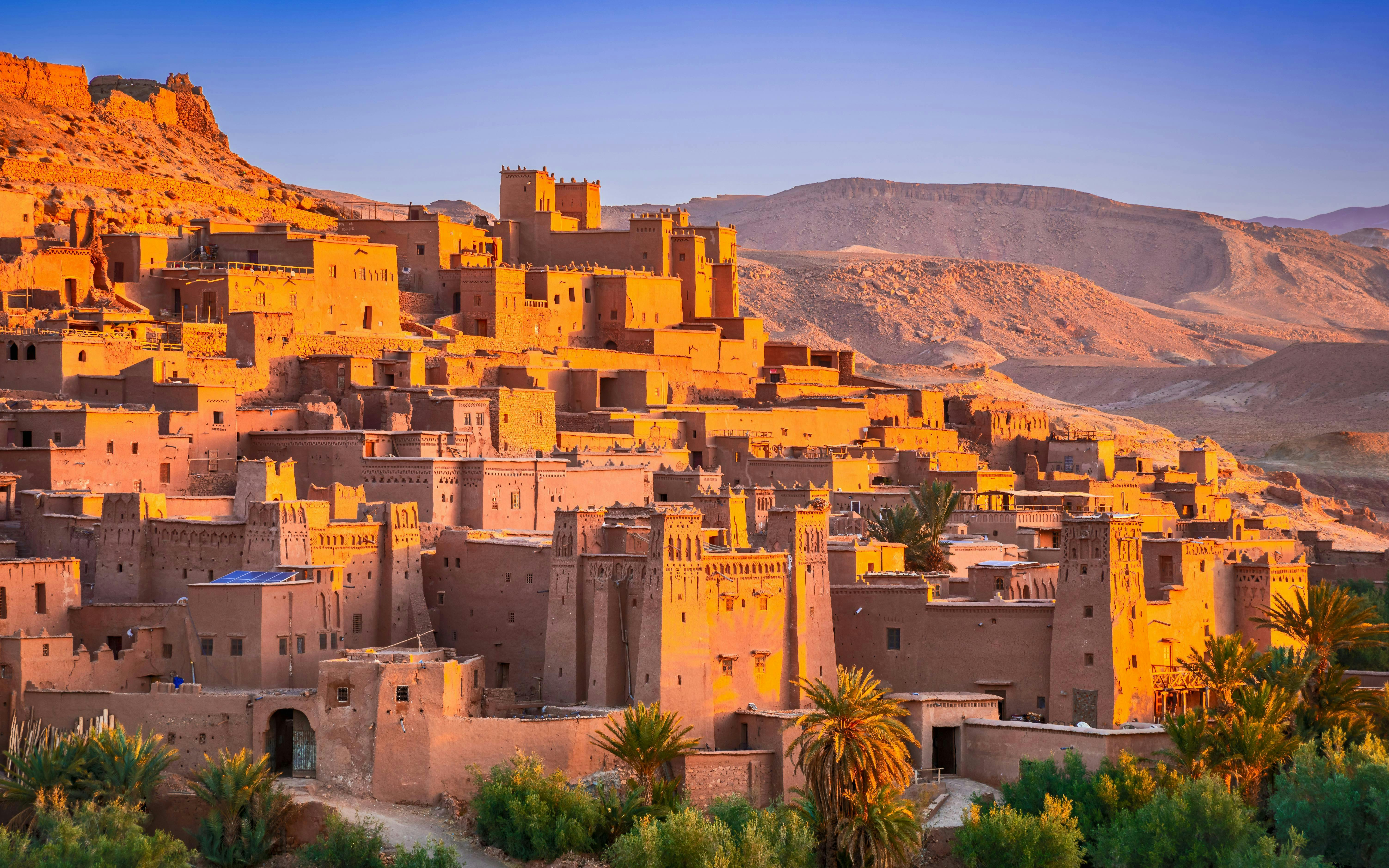 Ait Ben-Haddou kasbah with sunlit clay buildings in Morocco's desert landscape.