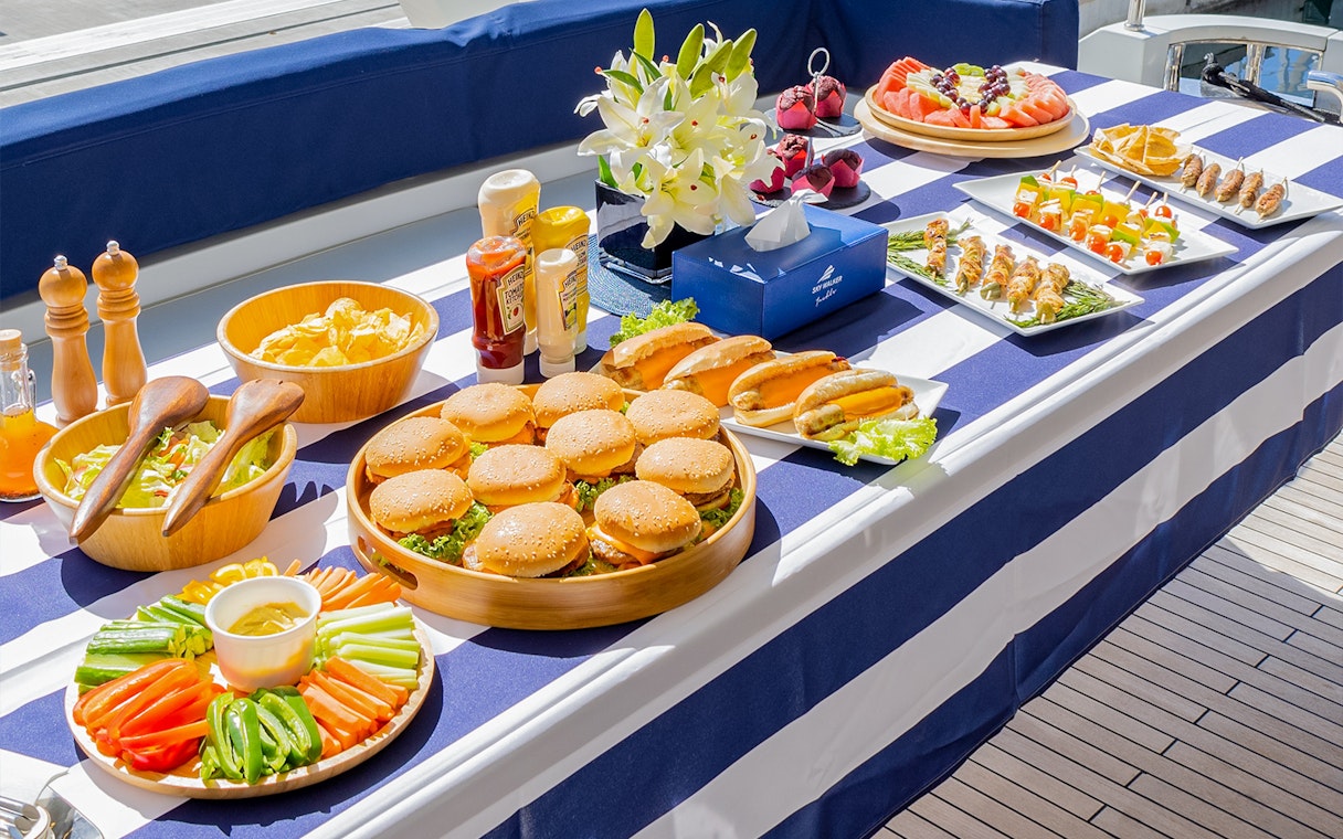 BBQ lunch spread on a yacht in Dubai with burgers, hot dogs, and salads.