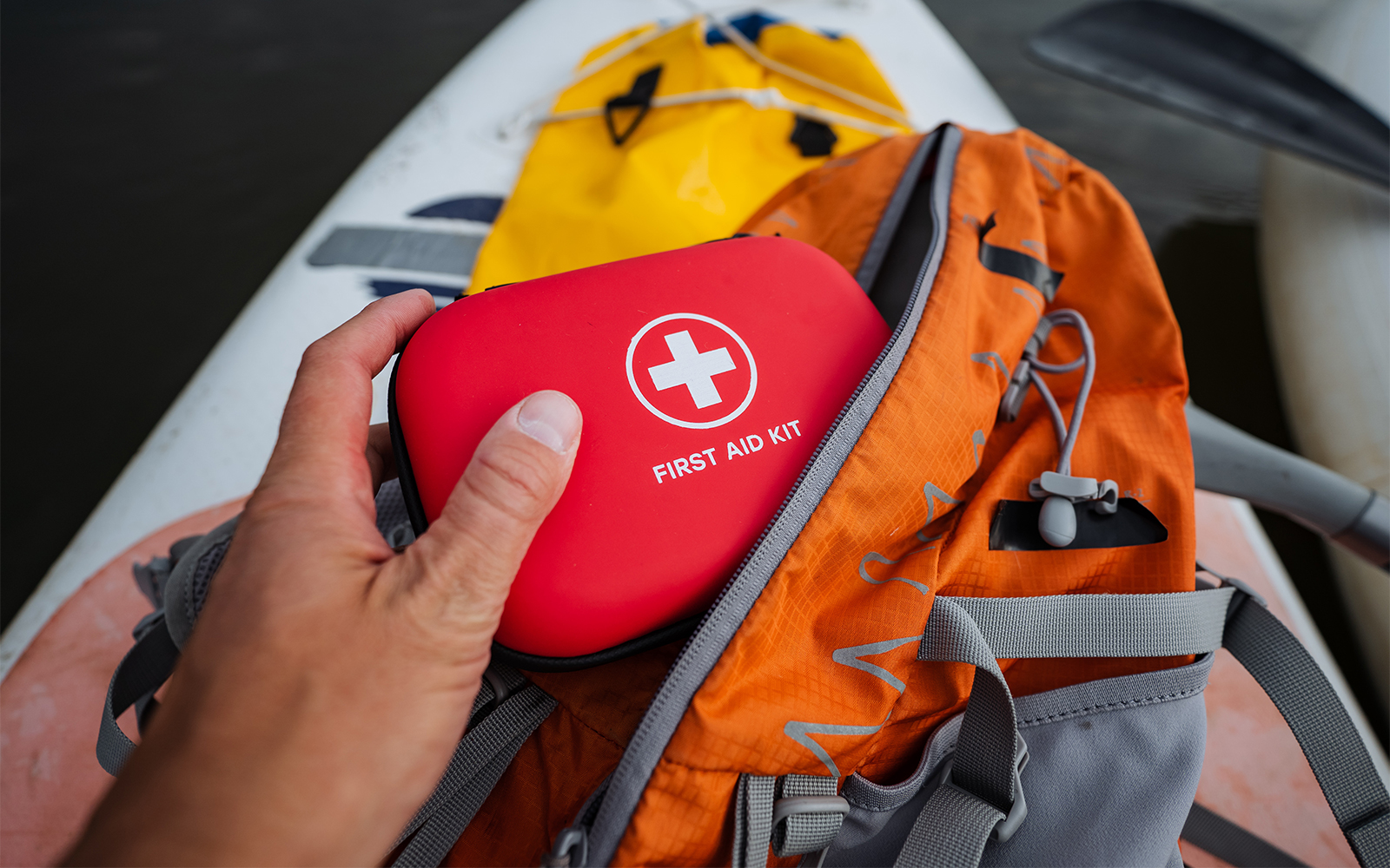 First aid kit being taken from an orange backpack on a kayak.