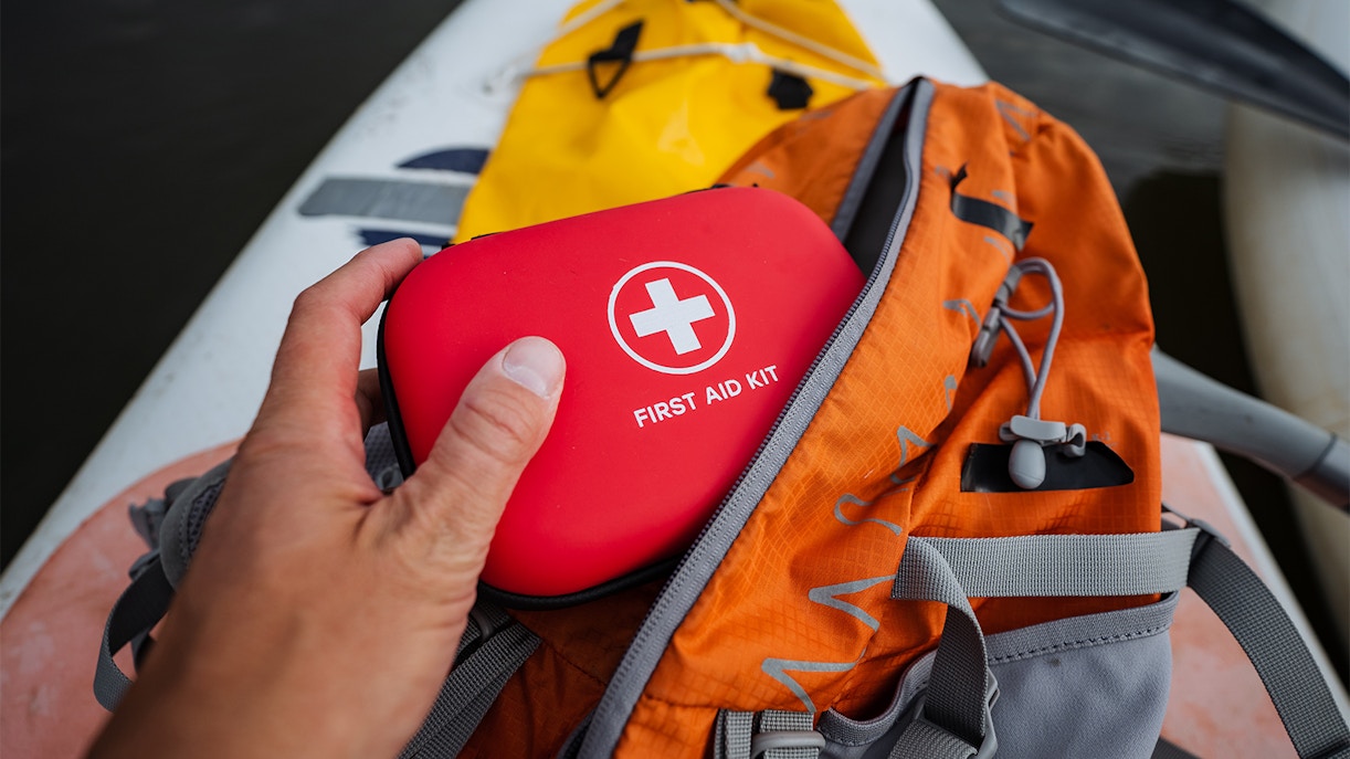 First aid kit being taken from an orange backpack on a kayak.
