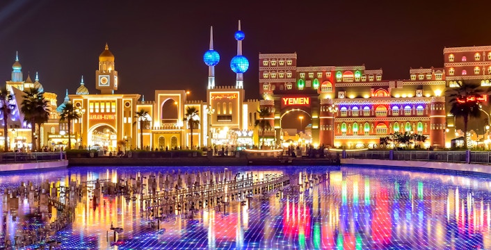 Global Village Dubai at night with illuminated pavilions and colorful reflections on water.