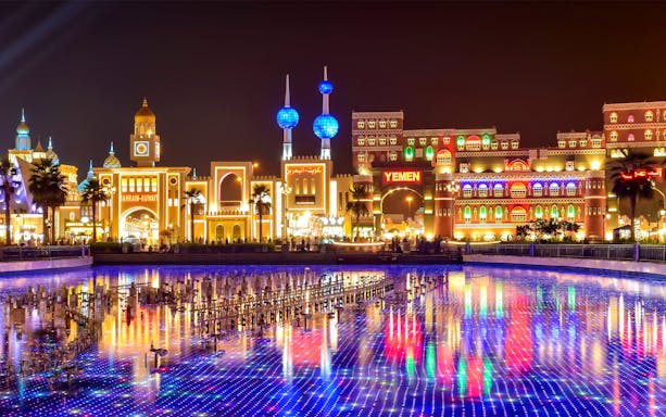 Global Village Dubai at night with illuminated pavilions and colorful reflections on water.