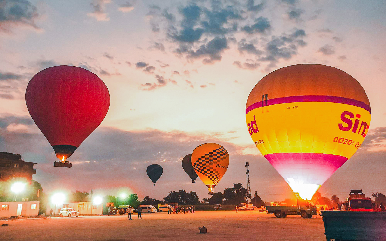 Hot air balloons preparing for takeoff at sunrise in a scenic open field.