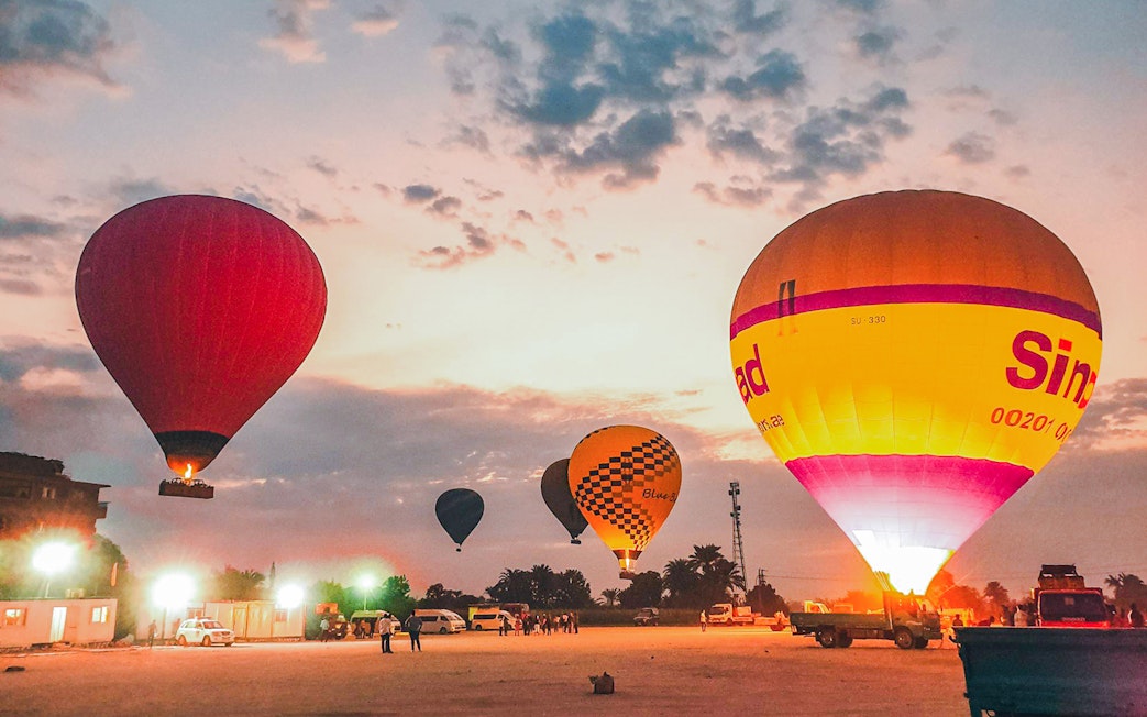 Hot air balloons preparing for takeoff at sunrise in a scenic open field.