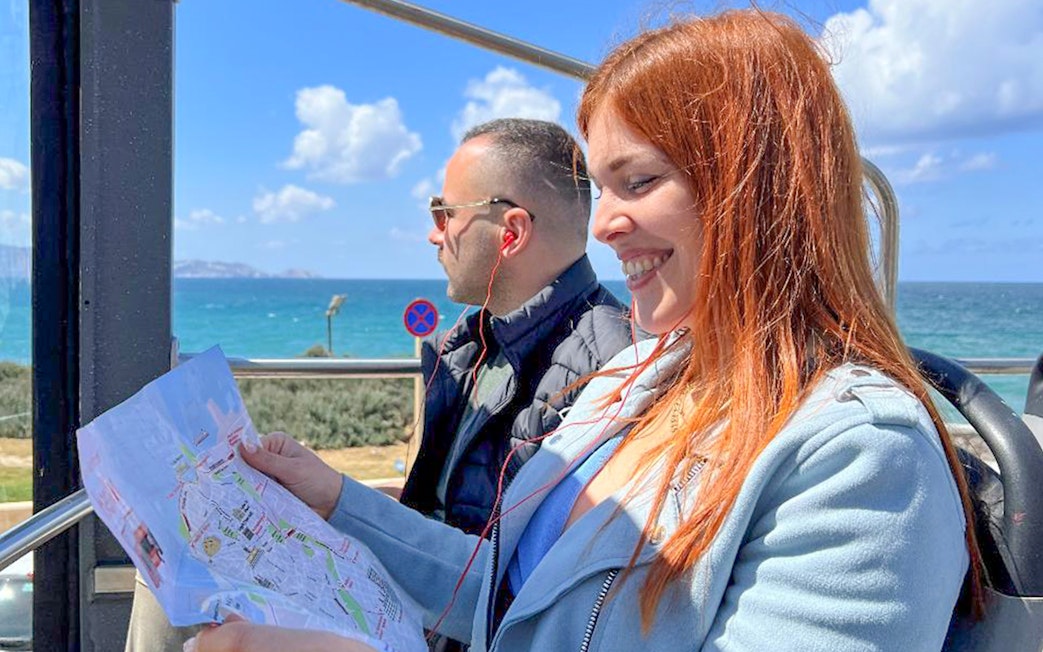 Tourists enjoying Heraklion Hop-On Hop-Off Bus Tour with sea view and map.