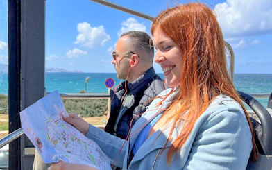 Tourists enjoying Heraklion Hop-On Hop-Off Bus Tour with sea view and map.