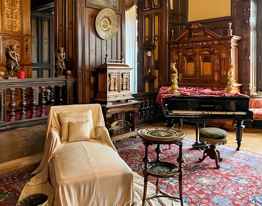Interior of Peles Castle with ornate woodwork, a grand piano, and elegant furnishings in Bucharest tour.