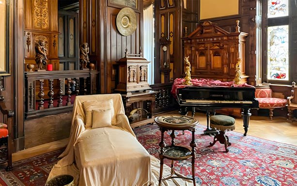 Interior of Peles Castle with ornate woodwork, a grand piano, and elegant furnishings in Bucharest tour.