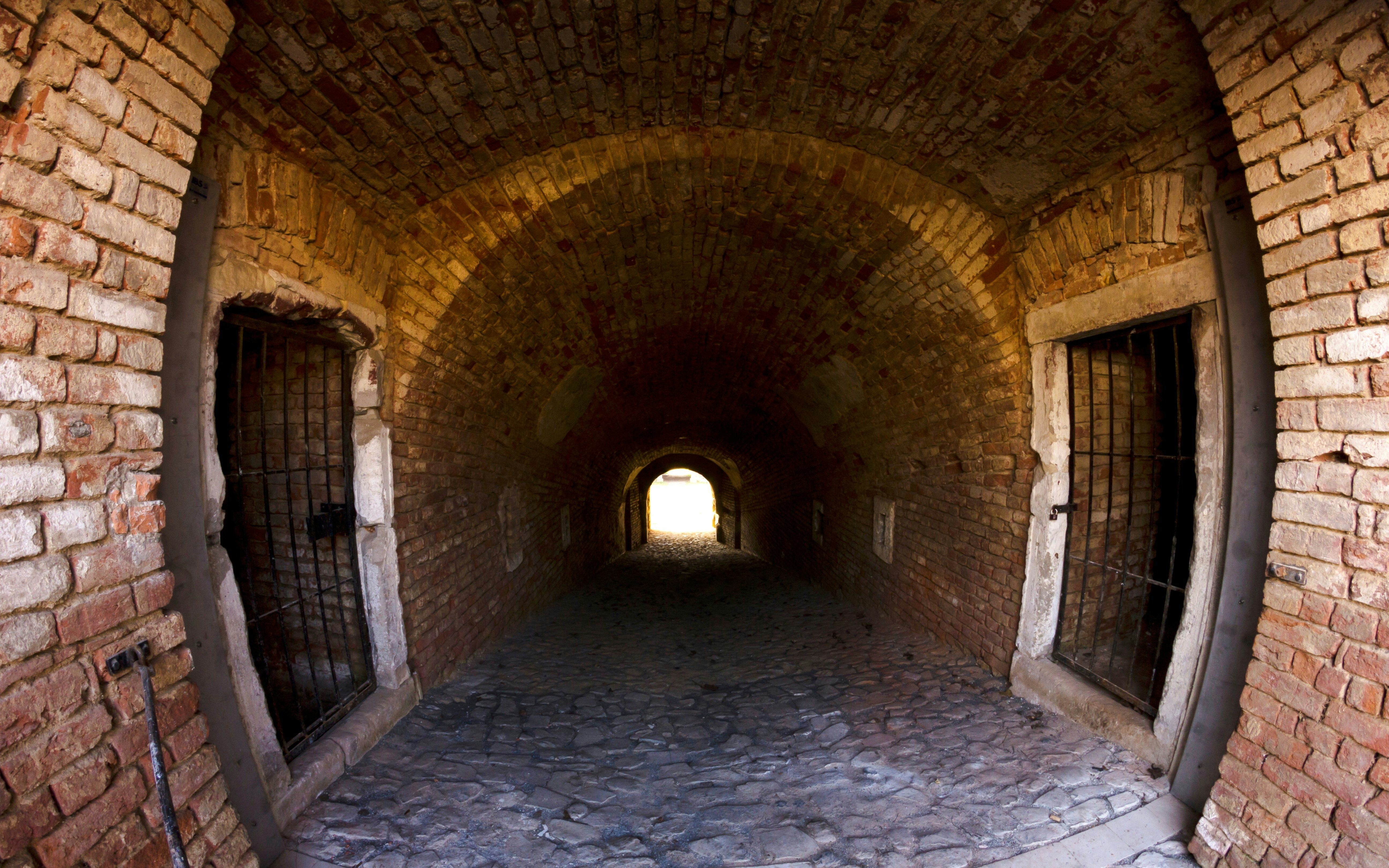 Brick tunnel at Terezín Concentration Camp with barred windows and cobblestone floor.