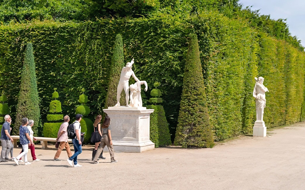 Tour guide leading group past statues in Garden of Versailles Palace, France.