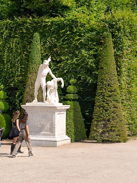 Tour guide leading group past statues in Garden of Versailles Palace, France.