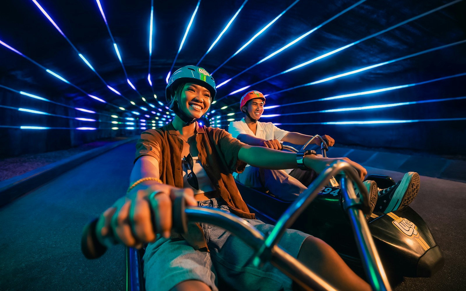 Friends enjoying night luge ride in illuminated tunnel, Singapore.