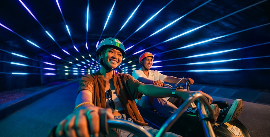 Friends enjoying night luge ride in illuminated tunnel, Singapore.