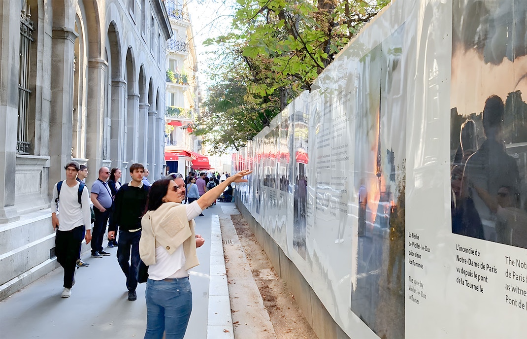 Visitors on a Notre Dame walking tour examining historical displays along a Paris street.