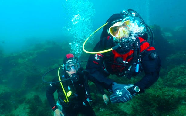 Scuba divers exploring underwater near Cyclopean Isles, Sicily.