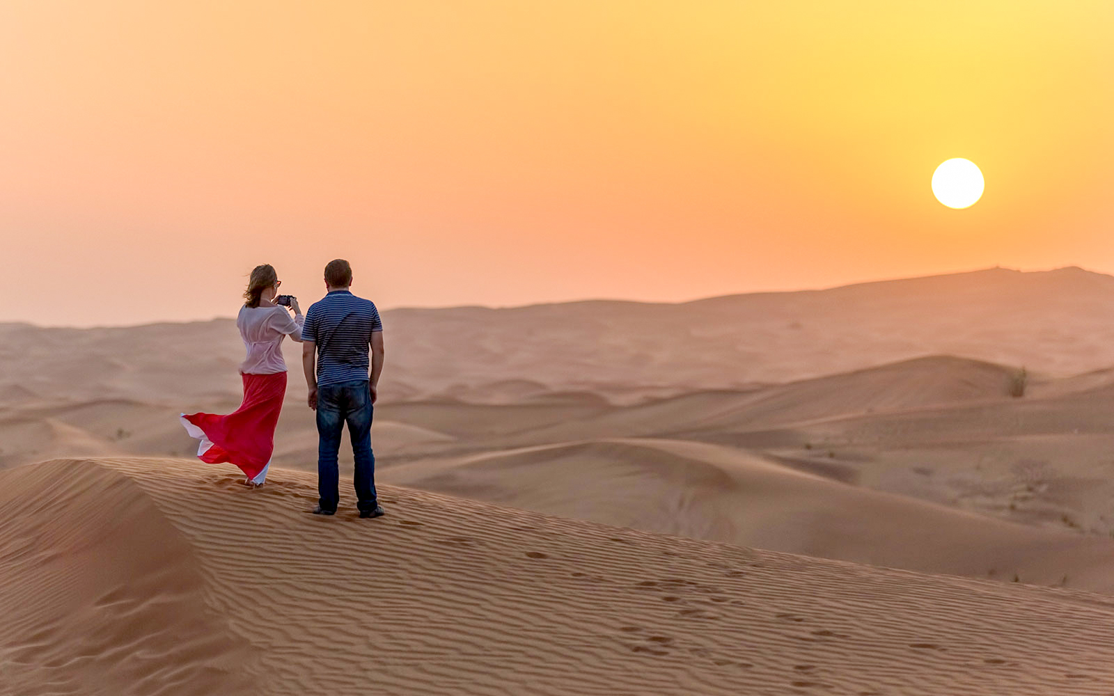 Couple watching sunset over desert dunes during evening safari adventure.