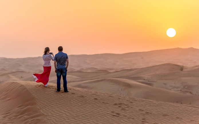 Couple watching sunset over desert dunes during evening safari adventure.