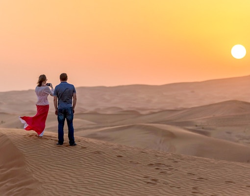 Couple watching sunset over desert dunes during evening safari adventure.