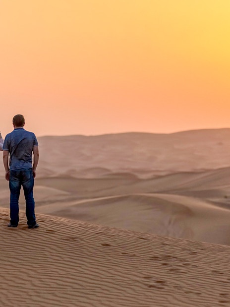 Couple watching sunset over desert dunes during evening safari adventure.