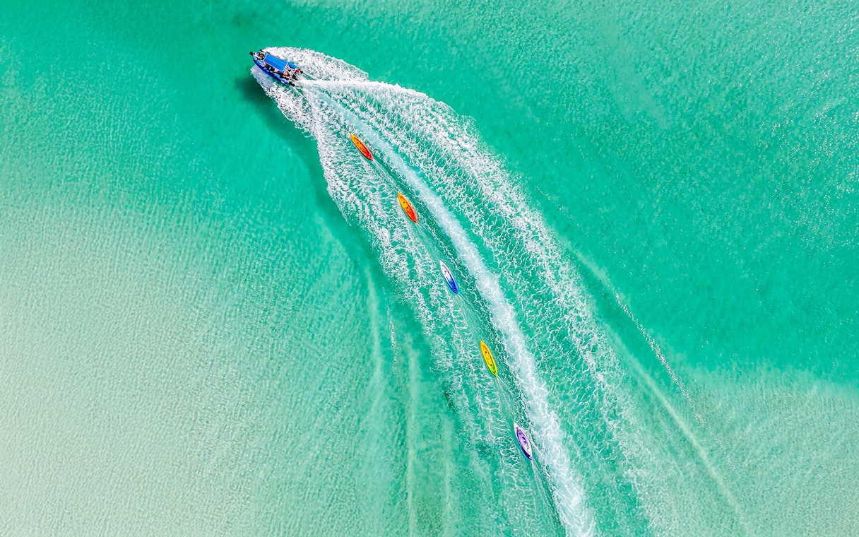 Aerial view of watersports activities on Fraser Island, K'gari, with kayaks trailing a speedboat.