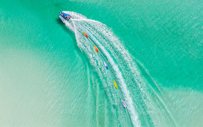 Aerial view of watersports activities on Fraser Island, K'gari, with kayaks trailing a speedboat.
