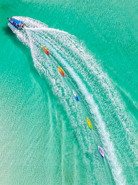 Aerial view of watersports activities on Fraser Island, K'gari, with kayaks trailing a speedboat.