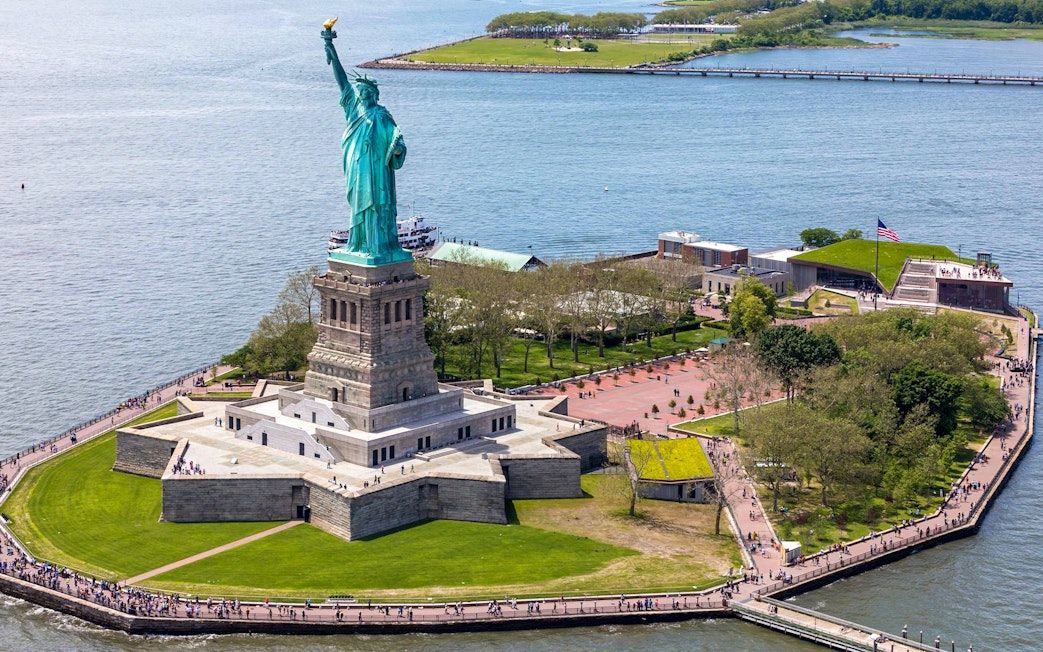 Statue of Liberty on Liberty Island with surrounding park and ferry dock.