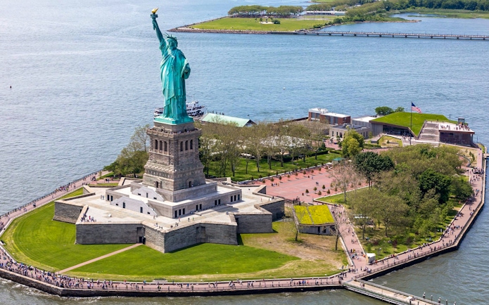 Statue of Liberty on Liberty Island with surrounding park and ferry dock.