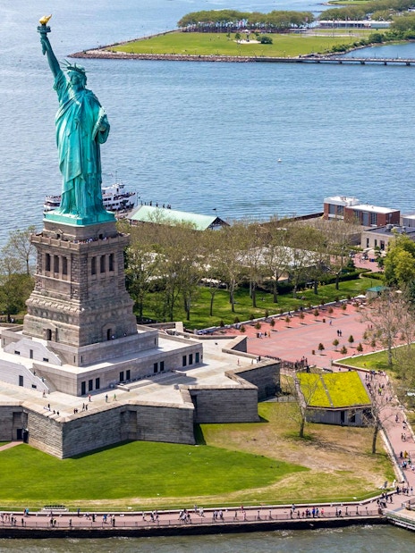 Statue of Liberty on Liberty Island with surrounding park and ferry dock.