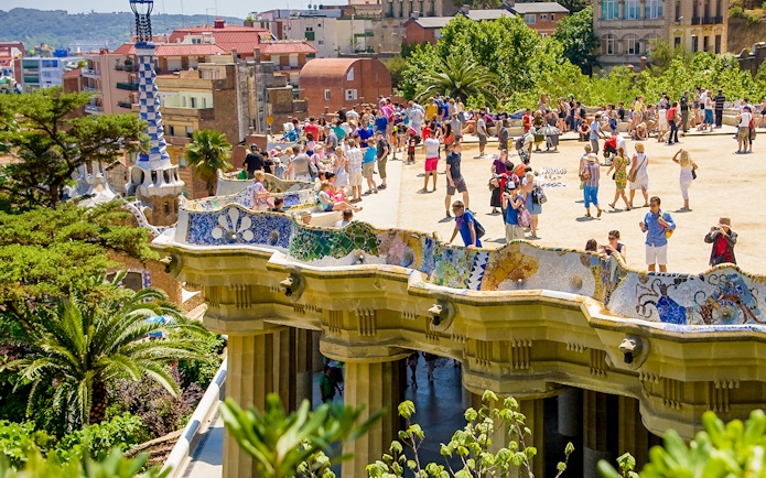 Park Güell terrace with colorful mosaic benches and tourists in Barcelona.