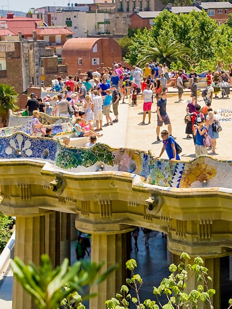 Park Güell terrace with colorful mosaic benches and tourists in Barcelona.