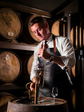 Man sampling whiskey from barrel in Irish distillery tour.