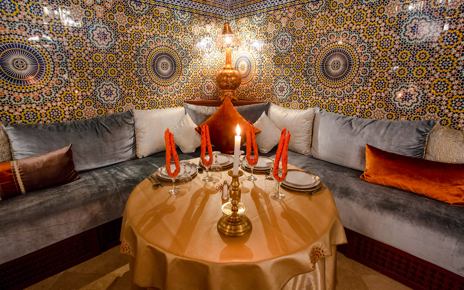 Moroccan dining setup with ornate tiles at Dar Essalam, featuring a candlelit table and plush seating.