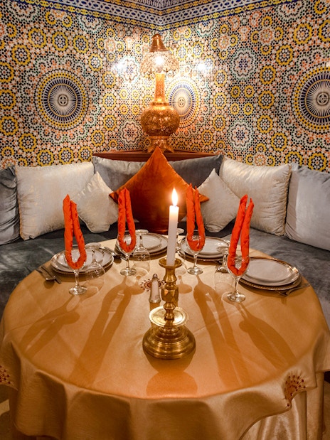 Moroccan dining setup with ornate tiles at Dar Essalam, featuring a candlelit table and plush seating.