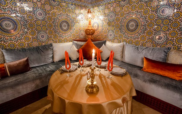 Moroccan dining setup with ornate tiles at Dar Essalam, featuring a candlelit table and plush seating.