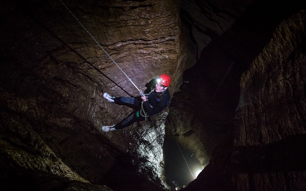 Person abseiling in a dark cave during a guided black water rafting experience in Waitomo.