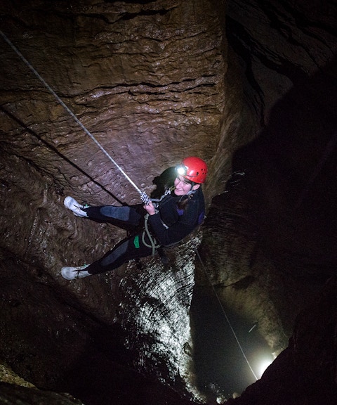 Person abseiling in a dark cave during a guided black water rafting experience in Waitomo.