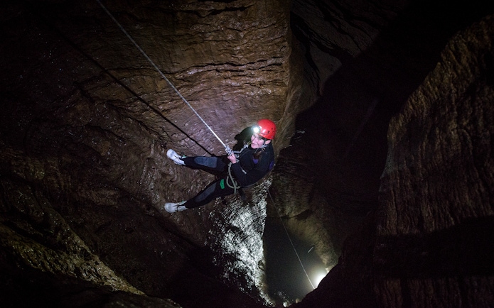 Person abseiling in a dark cave during a guided black water rafting experience in Waitomo.