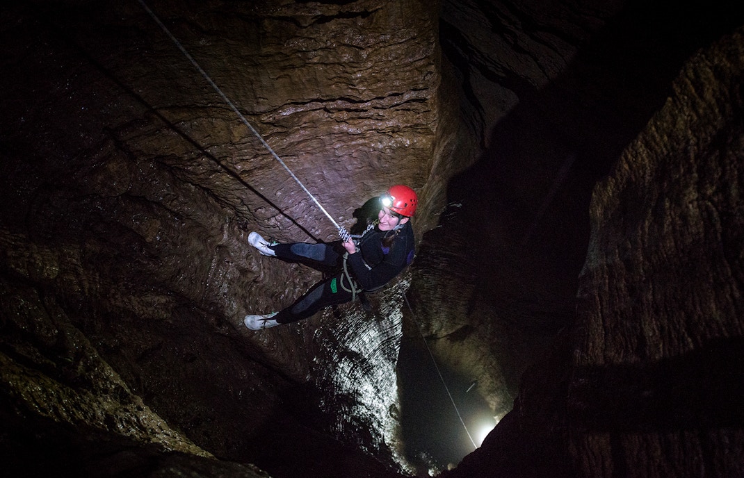 Person abseiling in a dark cave during a guided black water rafting experience in Waitomo.