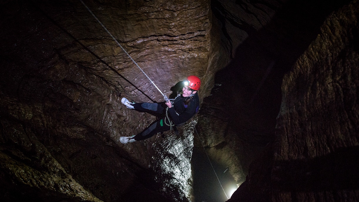 Person abseiling in a dark cave during a guided black water rafting experience in Waitomo.