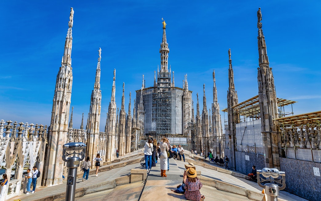 Tourists exploring the rooftop of Milan Duomo with spires in view.