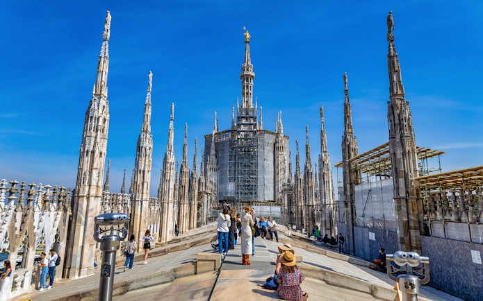 Tourists exploring the rooftop of Milan Duomo with spires in view.