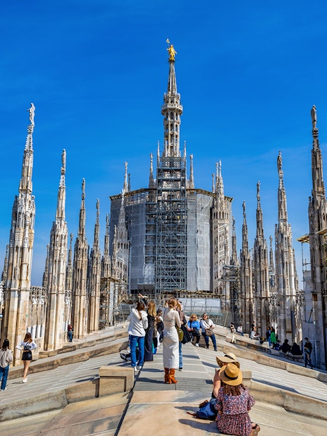 Tourists exploring the rooftop of Milan Duomo with spires in view.