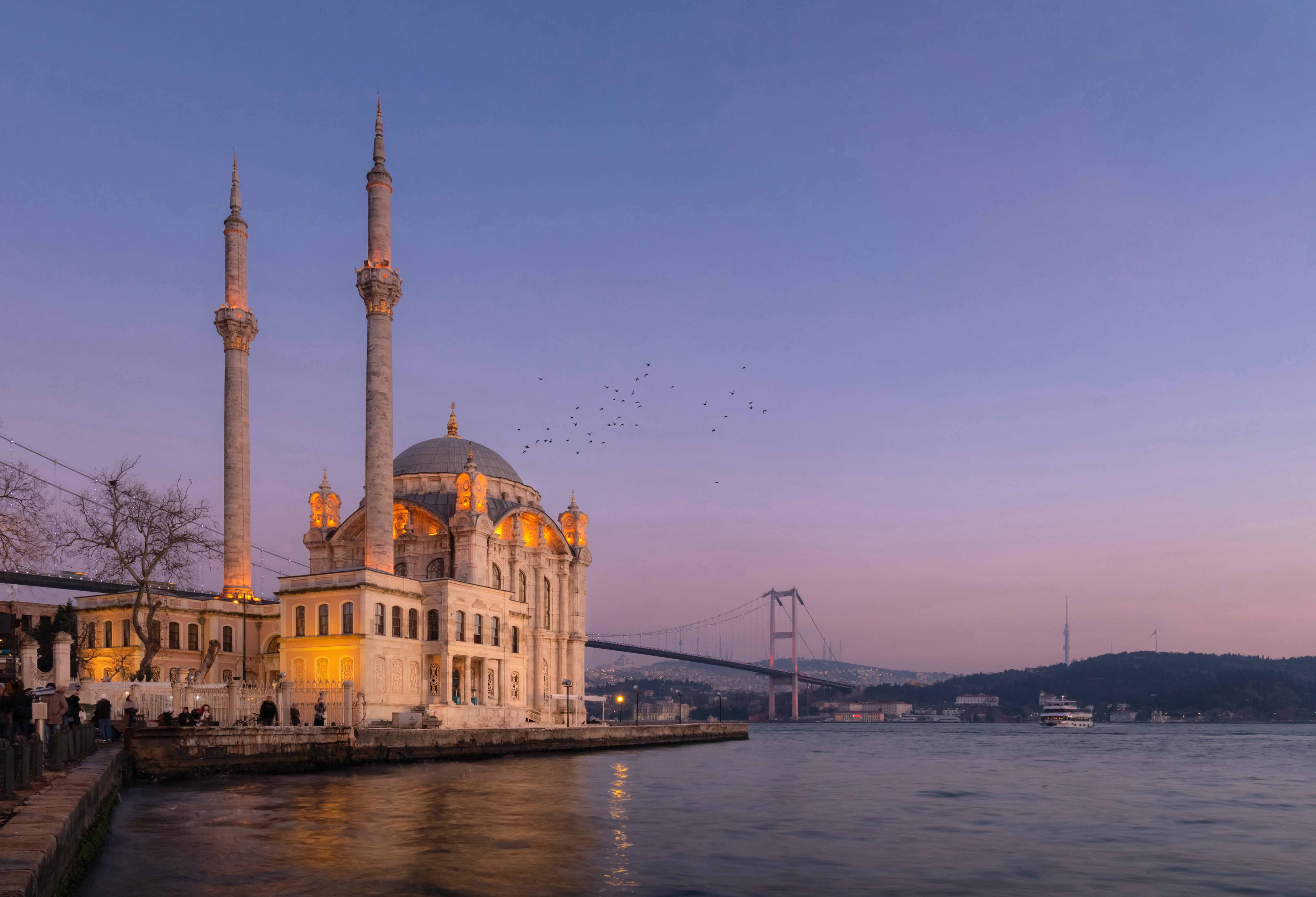 Ortaköy Mosque at sunset near Kabatas Pier, Istanbul, with Bosphorus Bridge in the background.