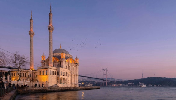 Ortaköy Mosque at sunset near Kabatas Pier, Istanbul, with Bosphorus Bridge in the background.