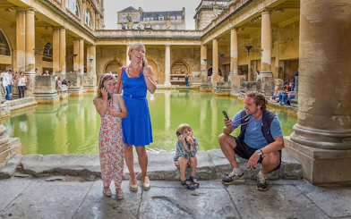 Tourists using audio guides at the Roman Baths in Bath, part of a day trip from London.